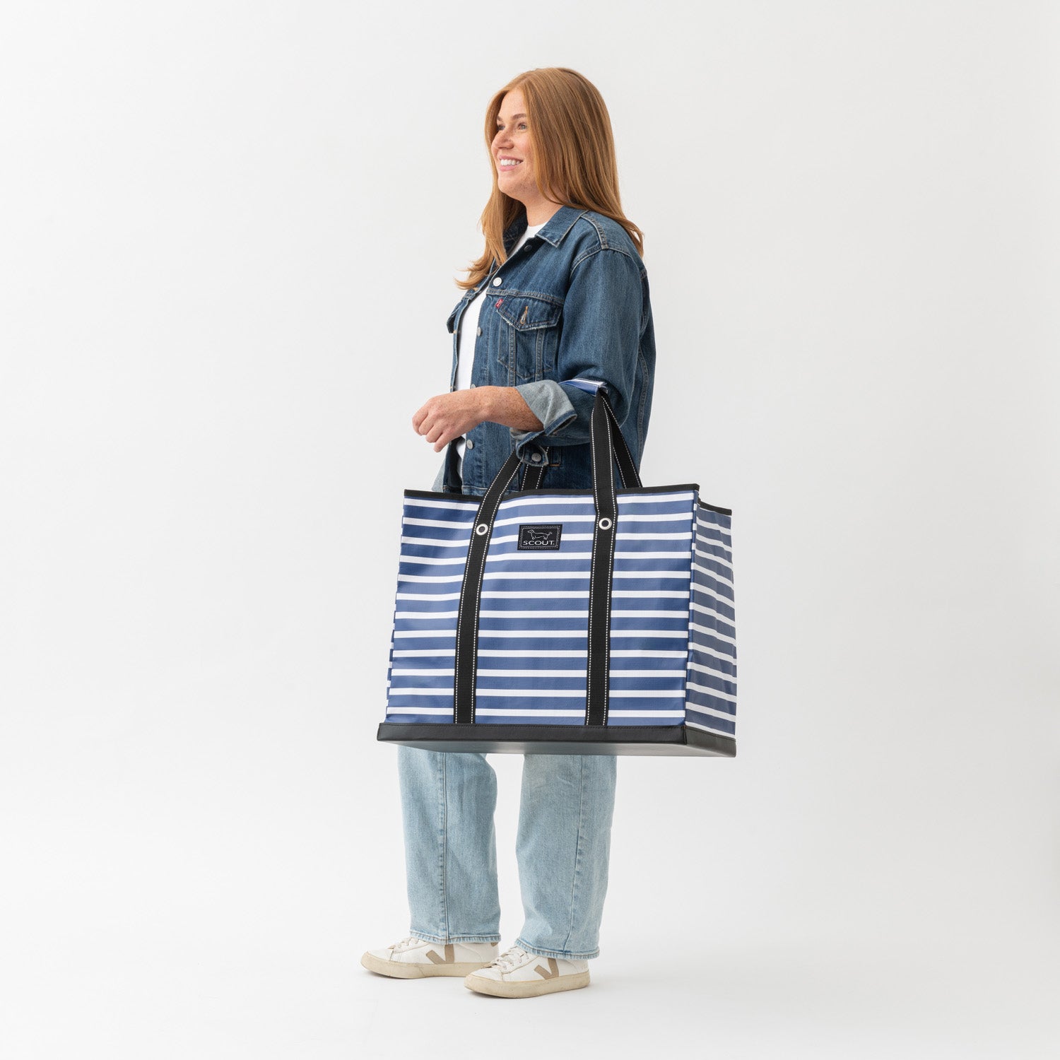 Woman holding a large blue and white striped tote bag against a white background