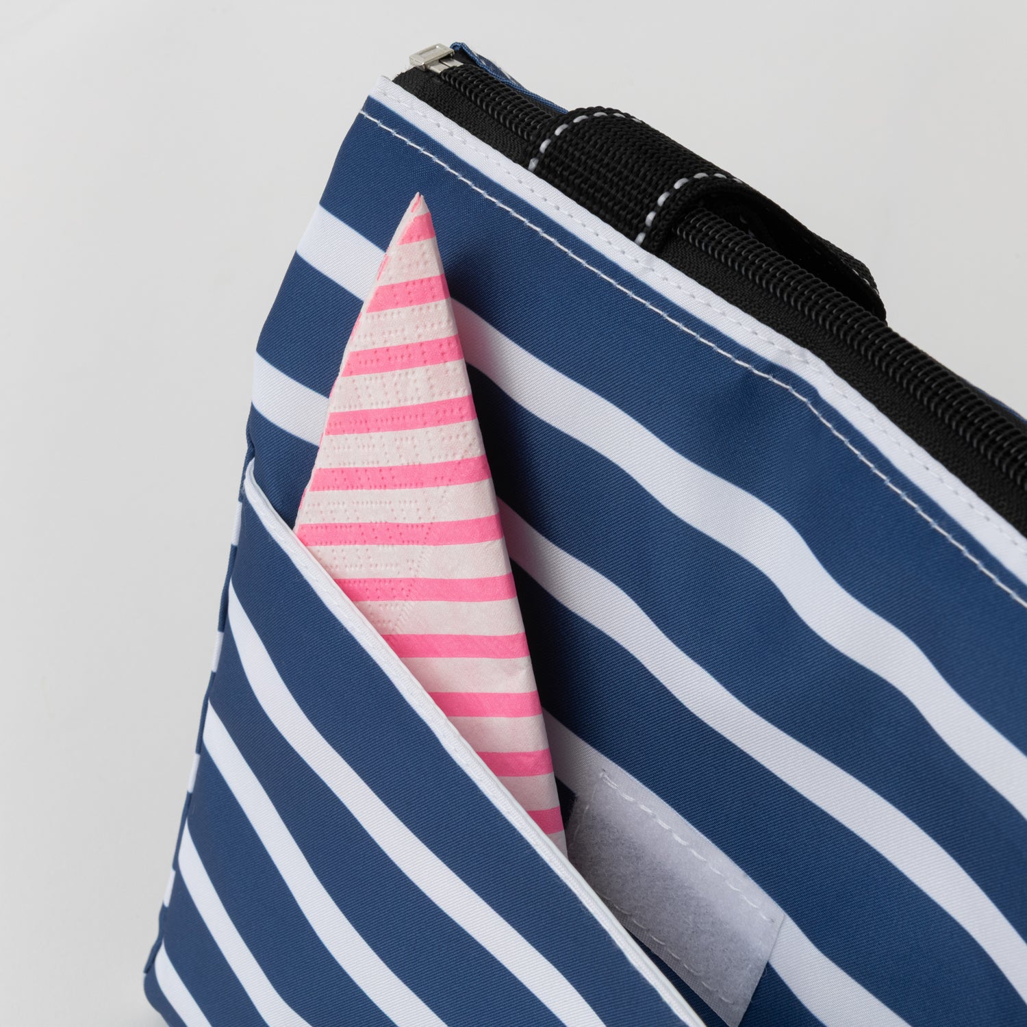 Close-up of a blue and white striped pouch with a pink and white striped napkin peeking out.