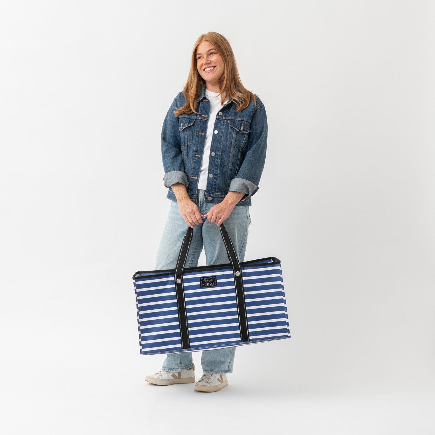 Woman holding a large blue and white striped tote bag against a white background