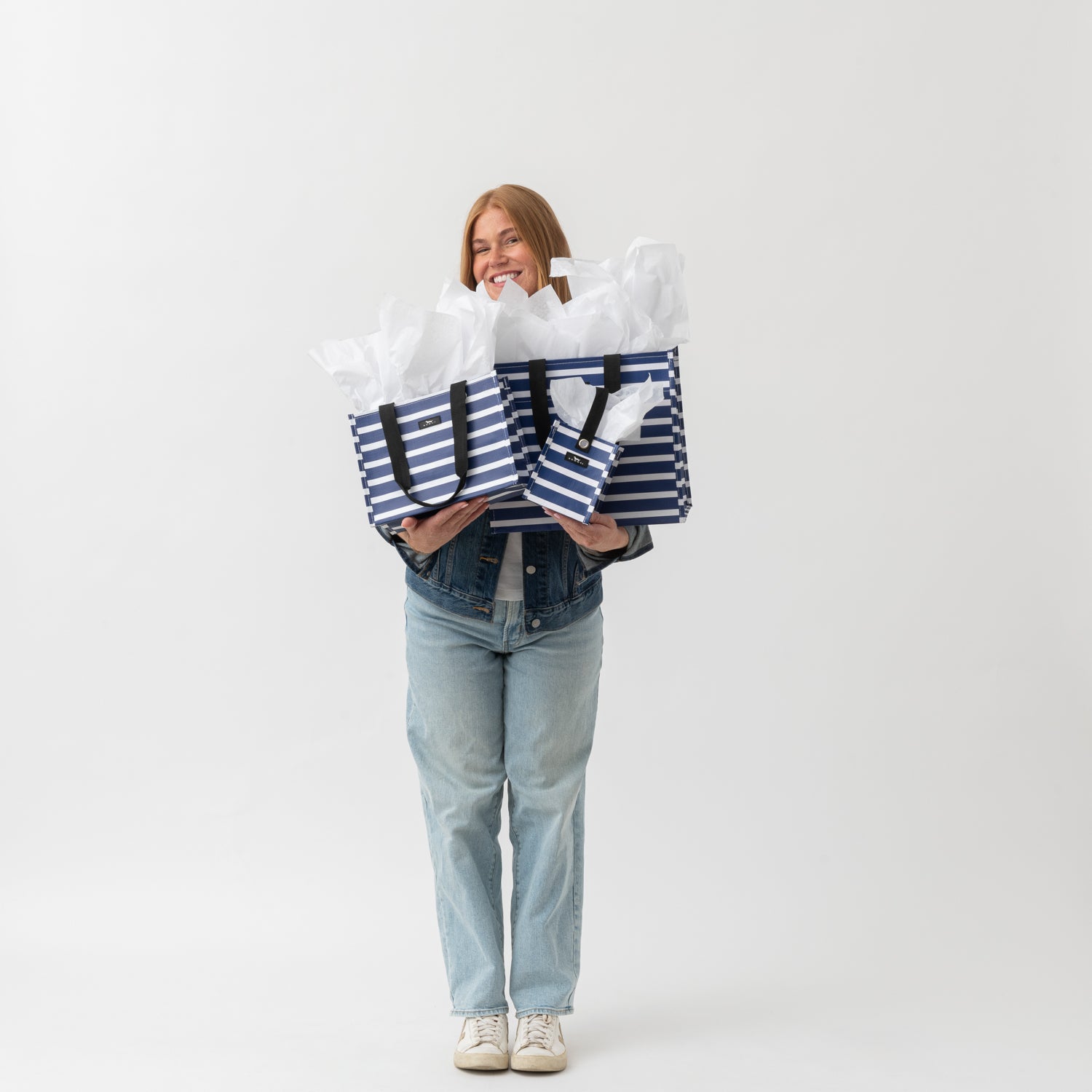Person holding two large striped bags against a white background