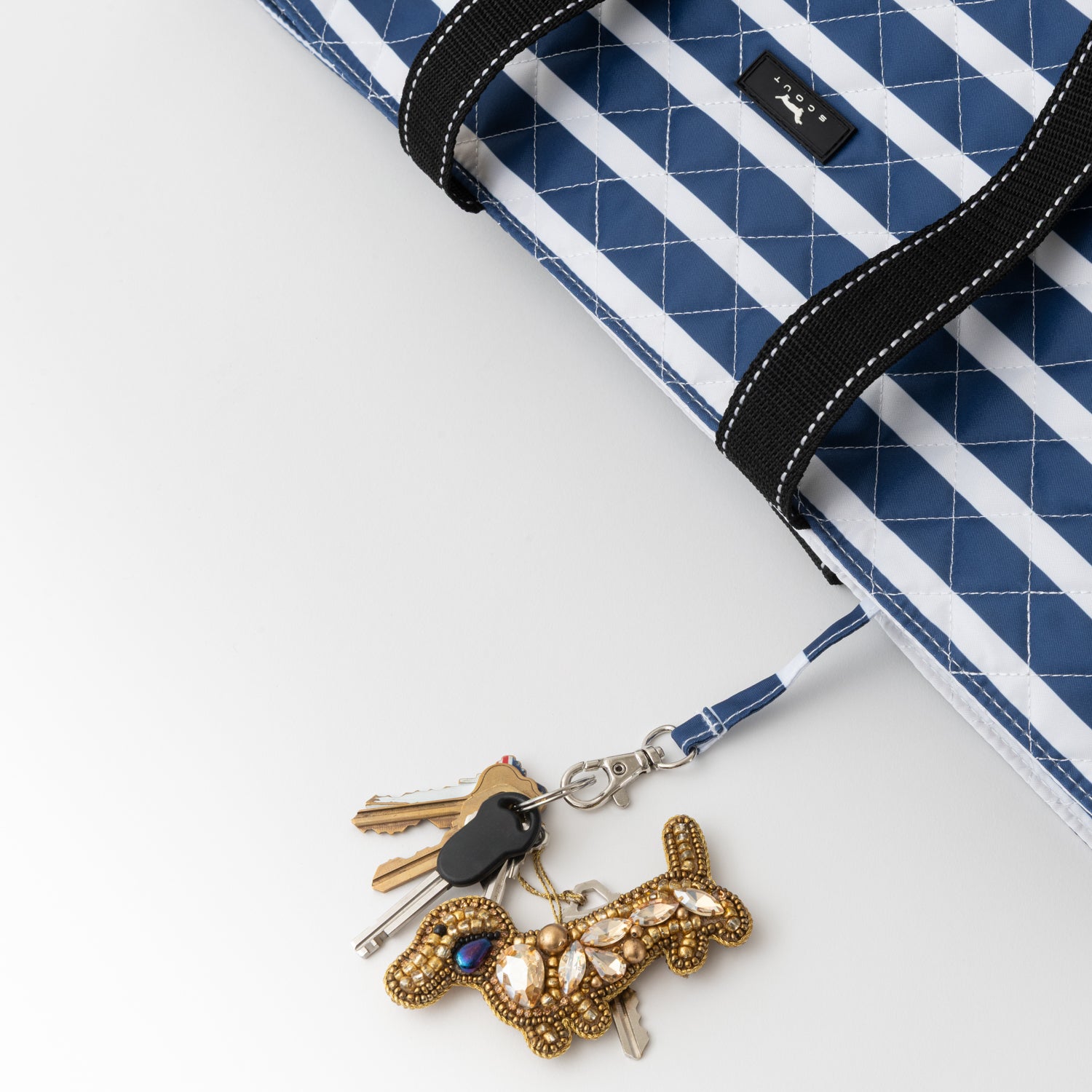 Keychain with decorative elements attached to a blue and white striped bag on a light gray background