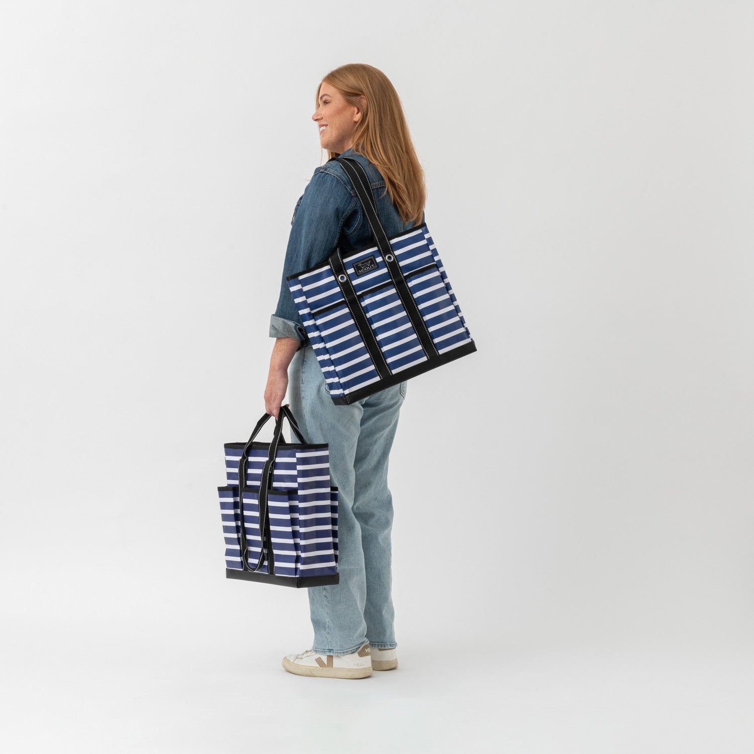 Woman holding two blue and white striped tote bags against a white background