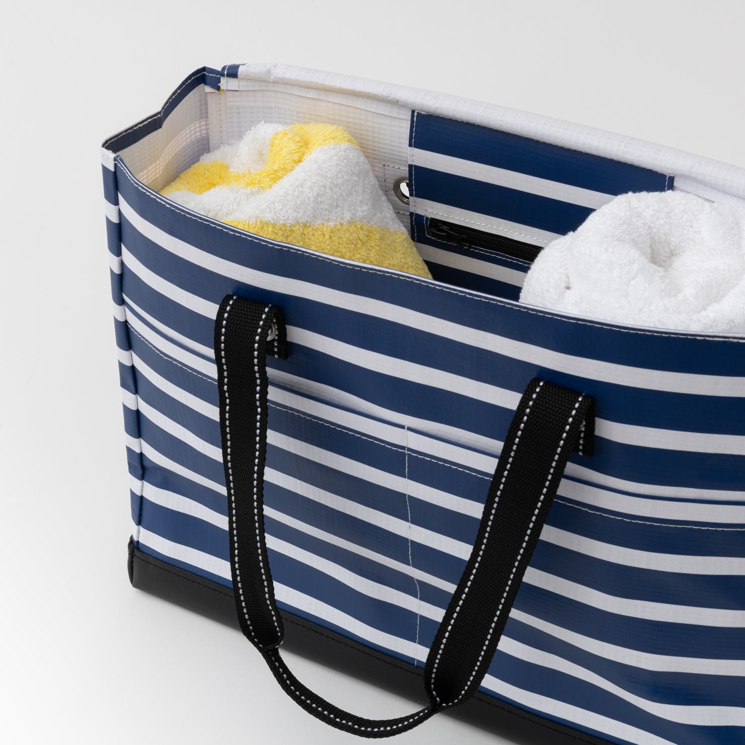 Blue and white striped tote bag with towels inside on a light gray background