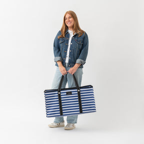 Woman holding a large blue and white striped tote bag against a white background