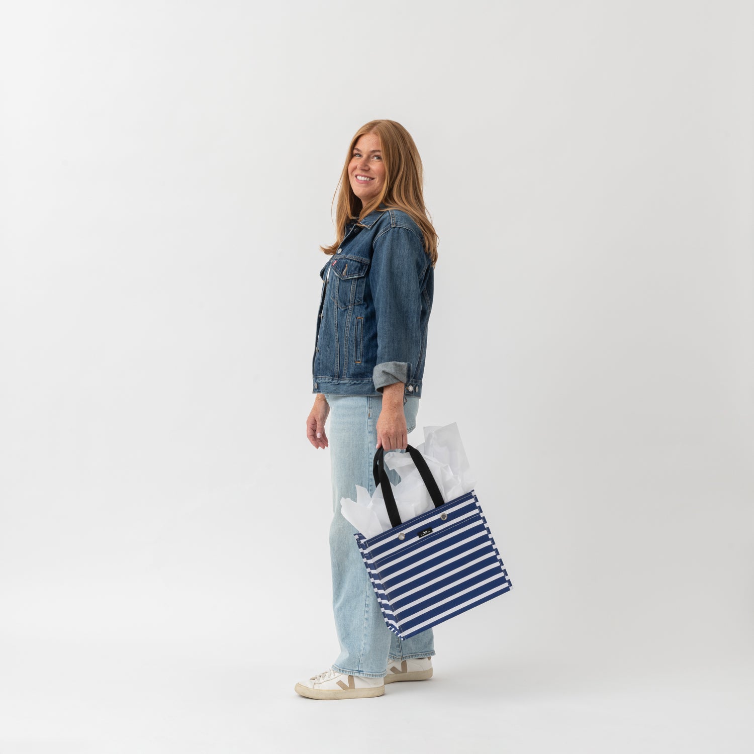 Woman holding a striped bag with groceries on a white background