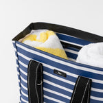 Blue and white striped tote bag with towels inside on a light gray background