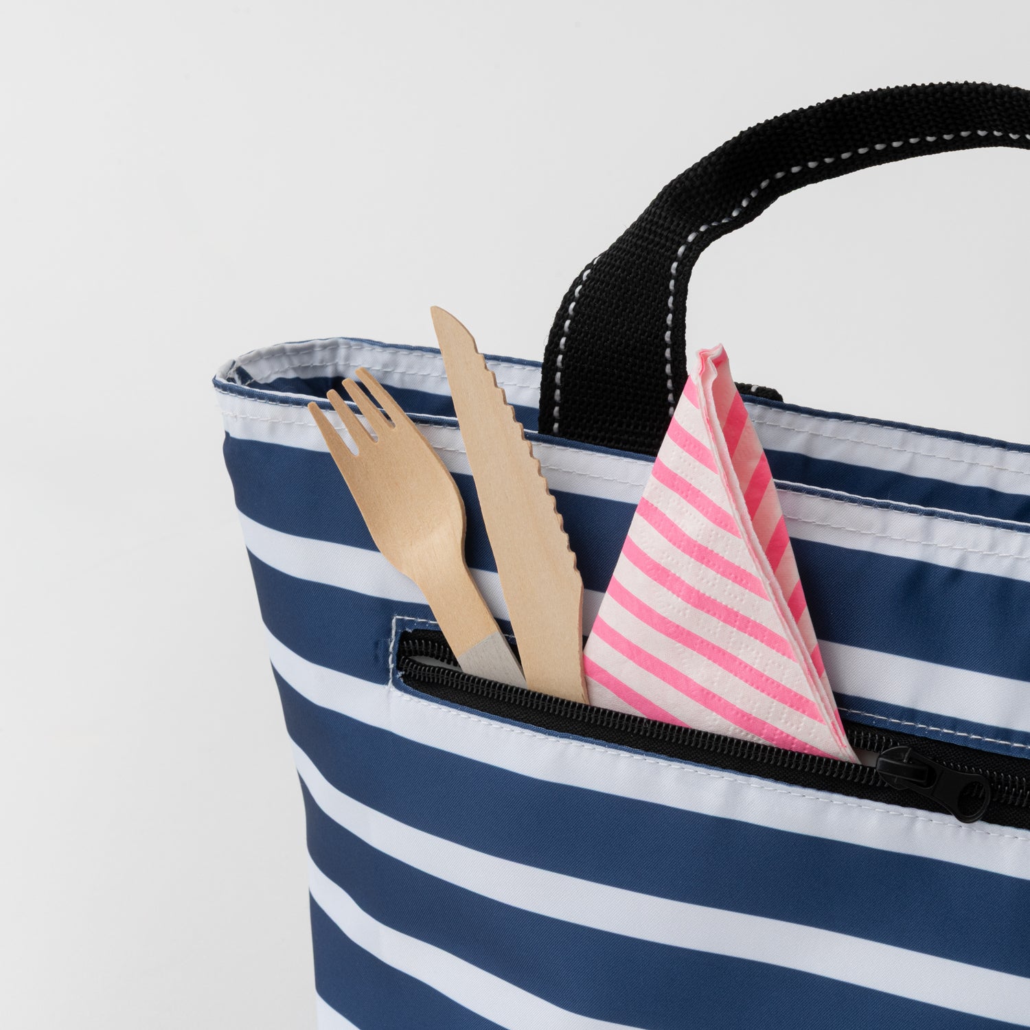 Navy and white striped tote bag with cutlery and a pink and white striped napkin on a light gray background