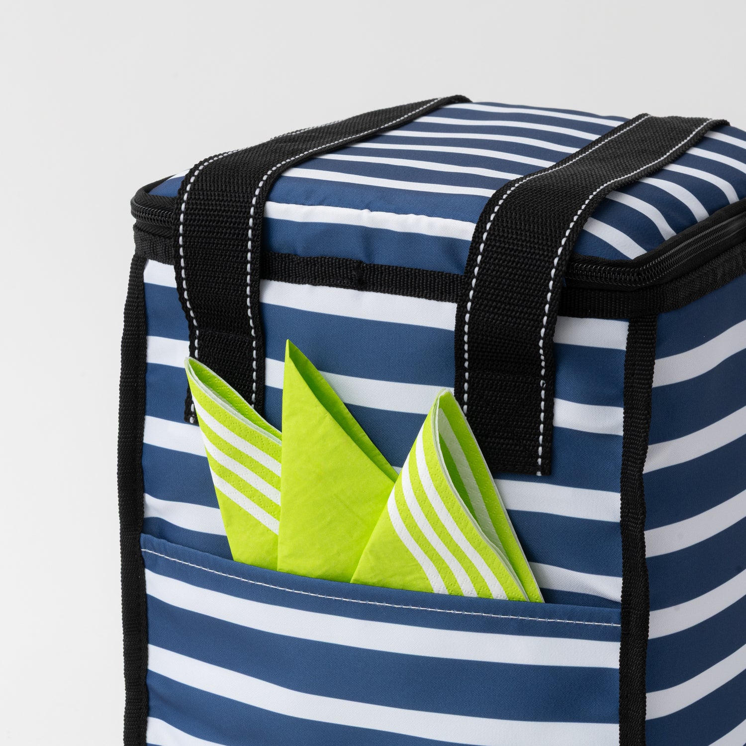 Blue and white striped cooler bag with green striped napkin peeking out of a pocket on a light gray background