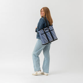 Woman carrying a blue and white striped tote bag on a plain background