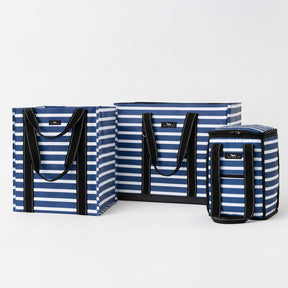 Three striped soft-sided bags in blue, navy, and white with black handles and trim, arranged on a light gray studio background.