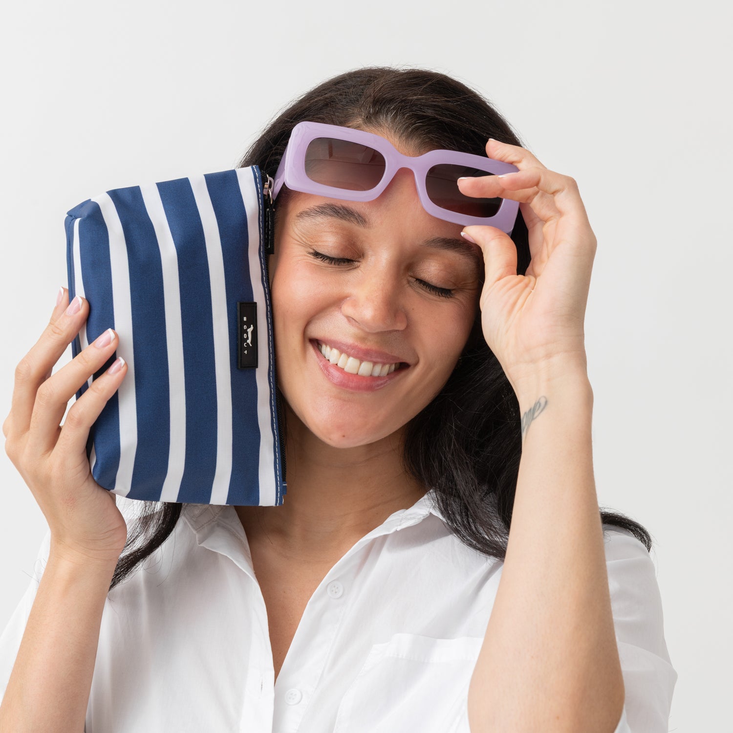 Woman holding a blue and white striped pouch with sunglasses on a plain background