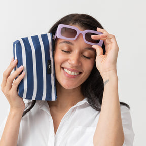 Woman holding a blue and white striped pouch with sunglasses on a plain background